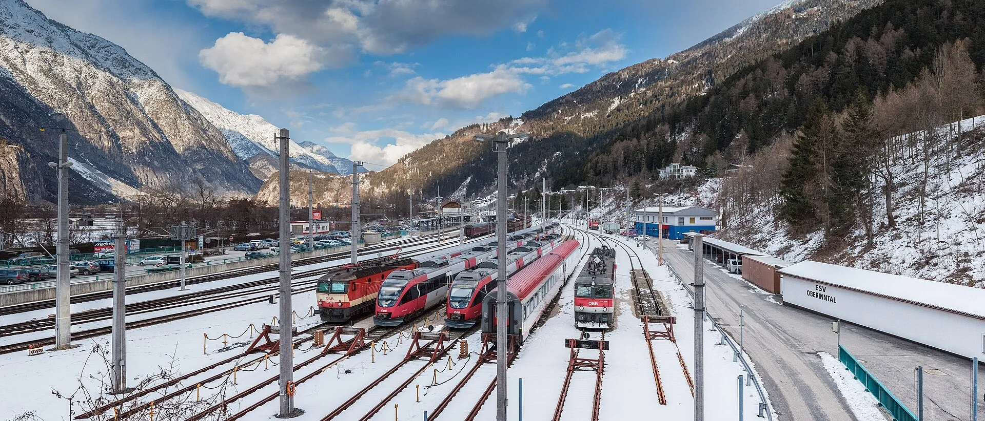 A panorama of Landeck-Zams station in winter with trains in the yard and snowy peaks behind.