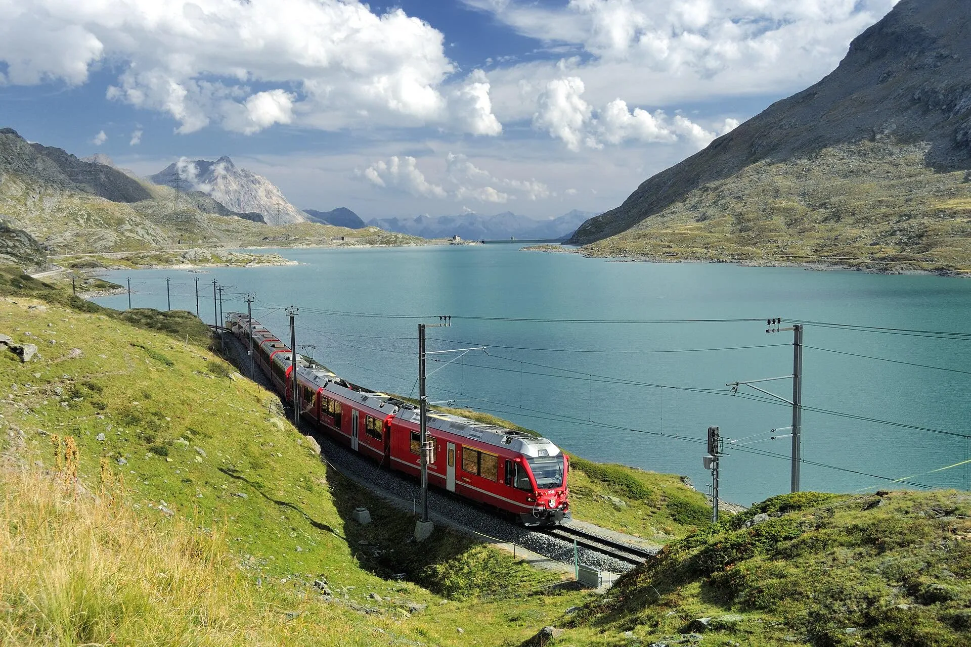 A red Allegra train running along the shore of Lago Bianco near the top of the Bernina Pass.