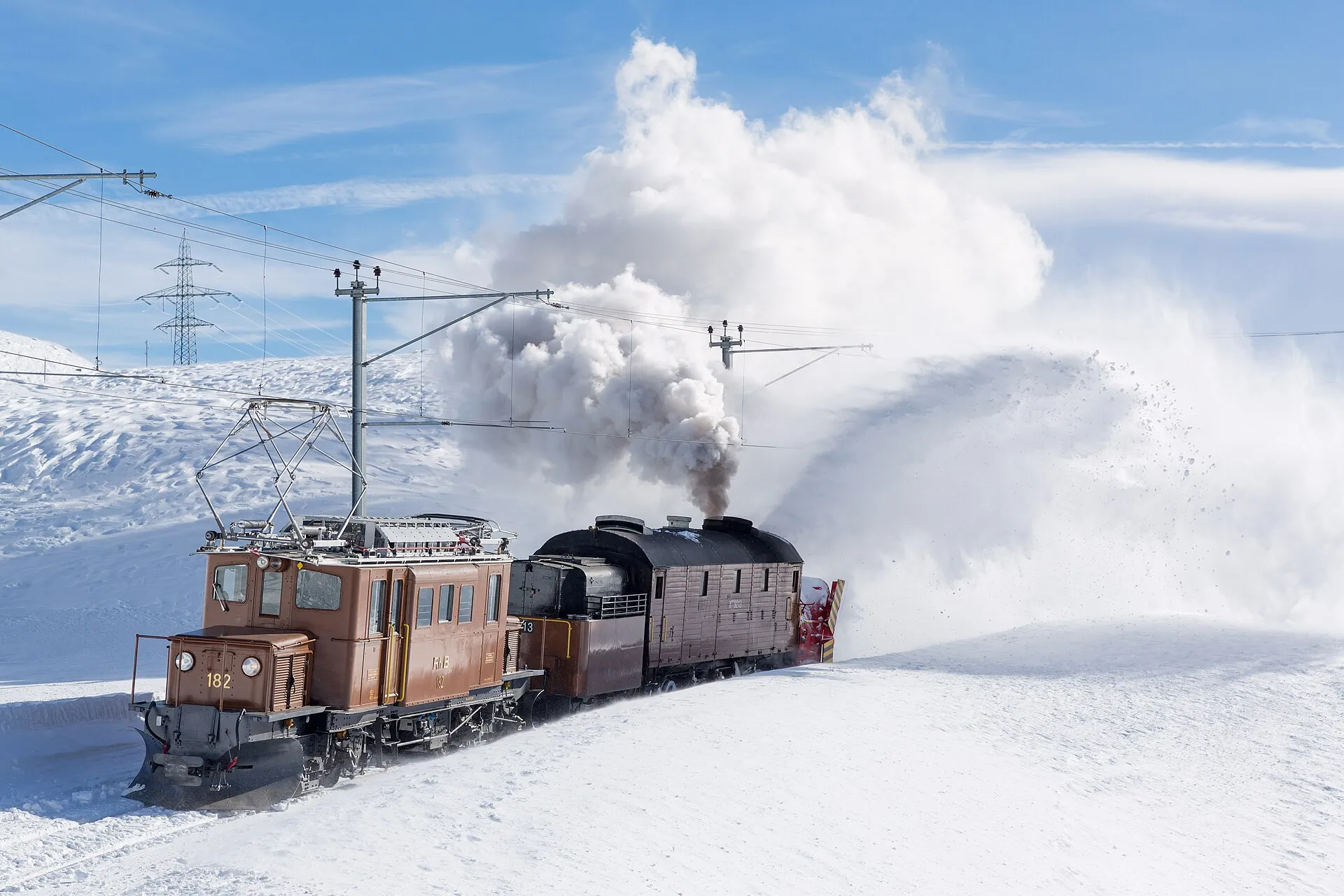 A historic Bernina crocodile locomotive and a steam rotary snow plough clearing snow on the Bernina Pass.