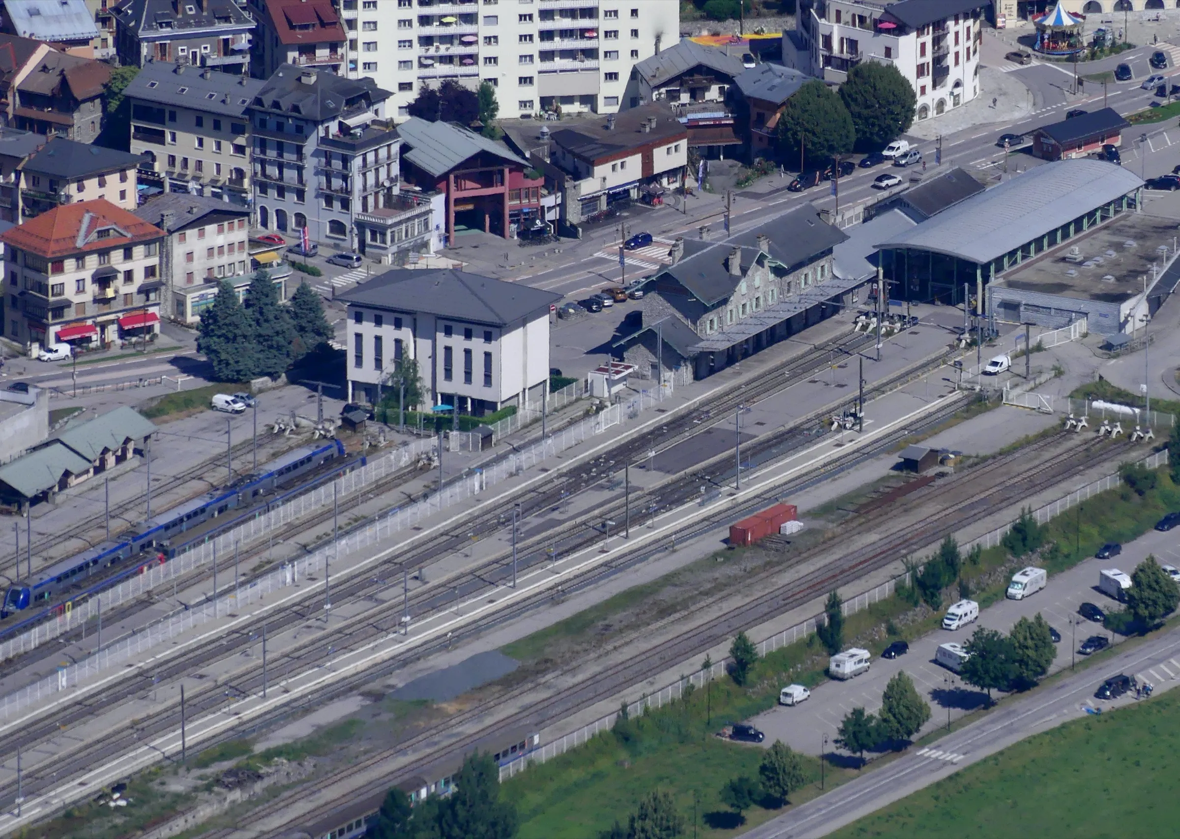 Bourg-Saint-Maurice station and its tracks seen from above on a summer morning, with a blue train at the platform.