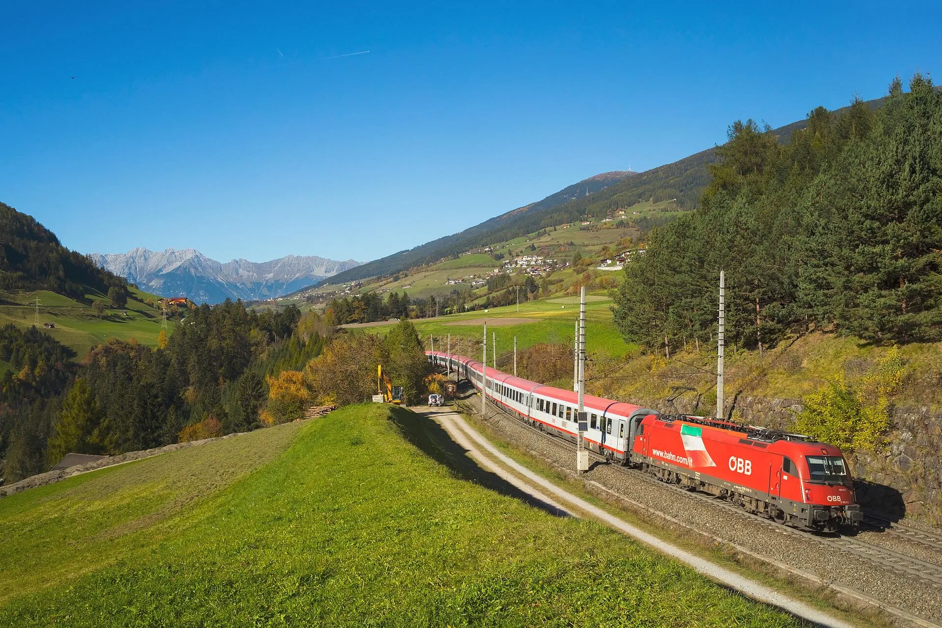 A Eurocity train climbing through green meadows in the Wipptal near Matrei am Brenner.