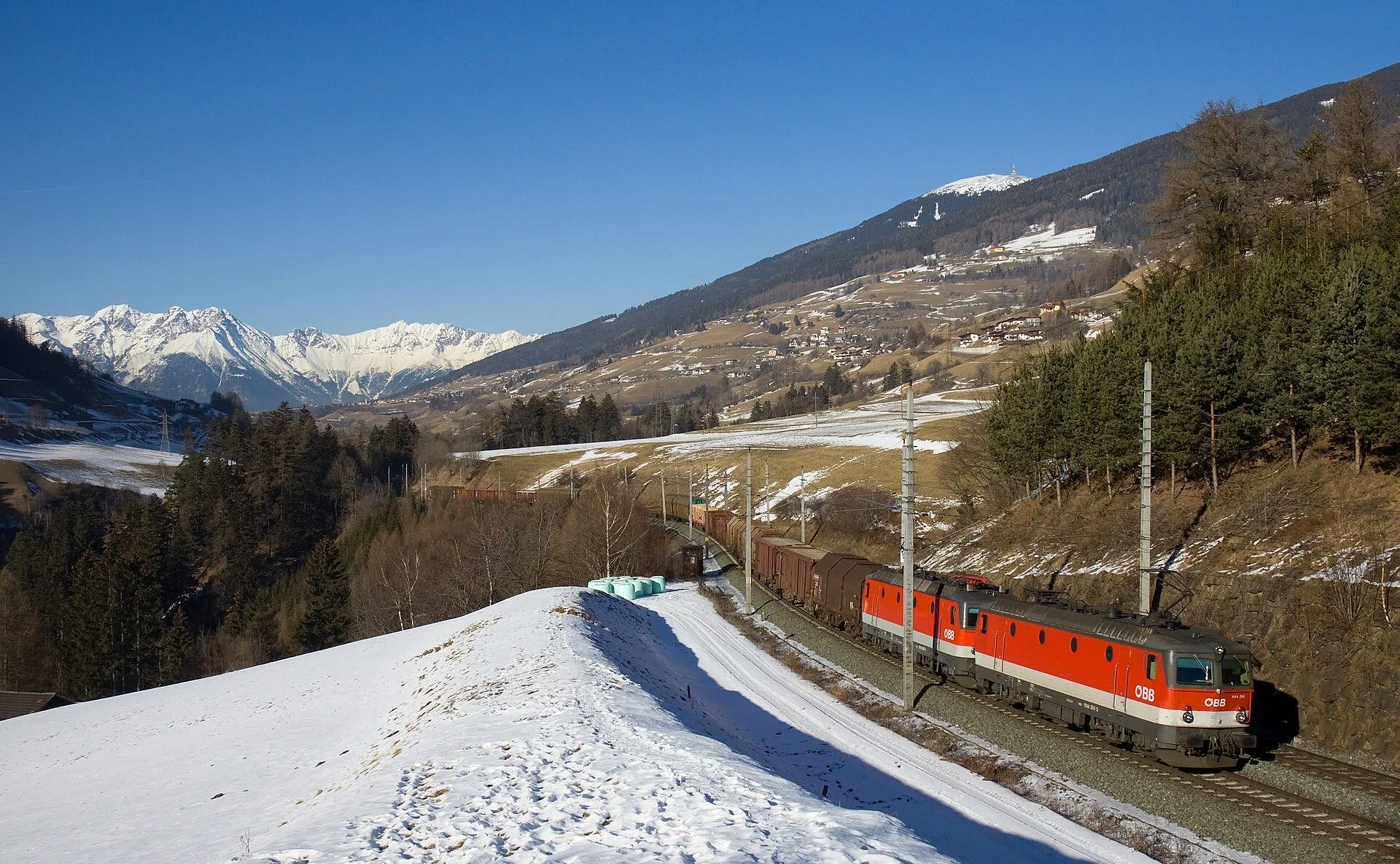 A red ÖBB locomotive hauling a train between Innsbruck and Matrei in late winter.