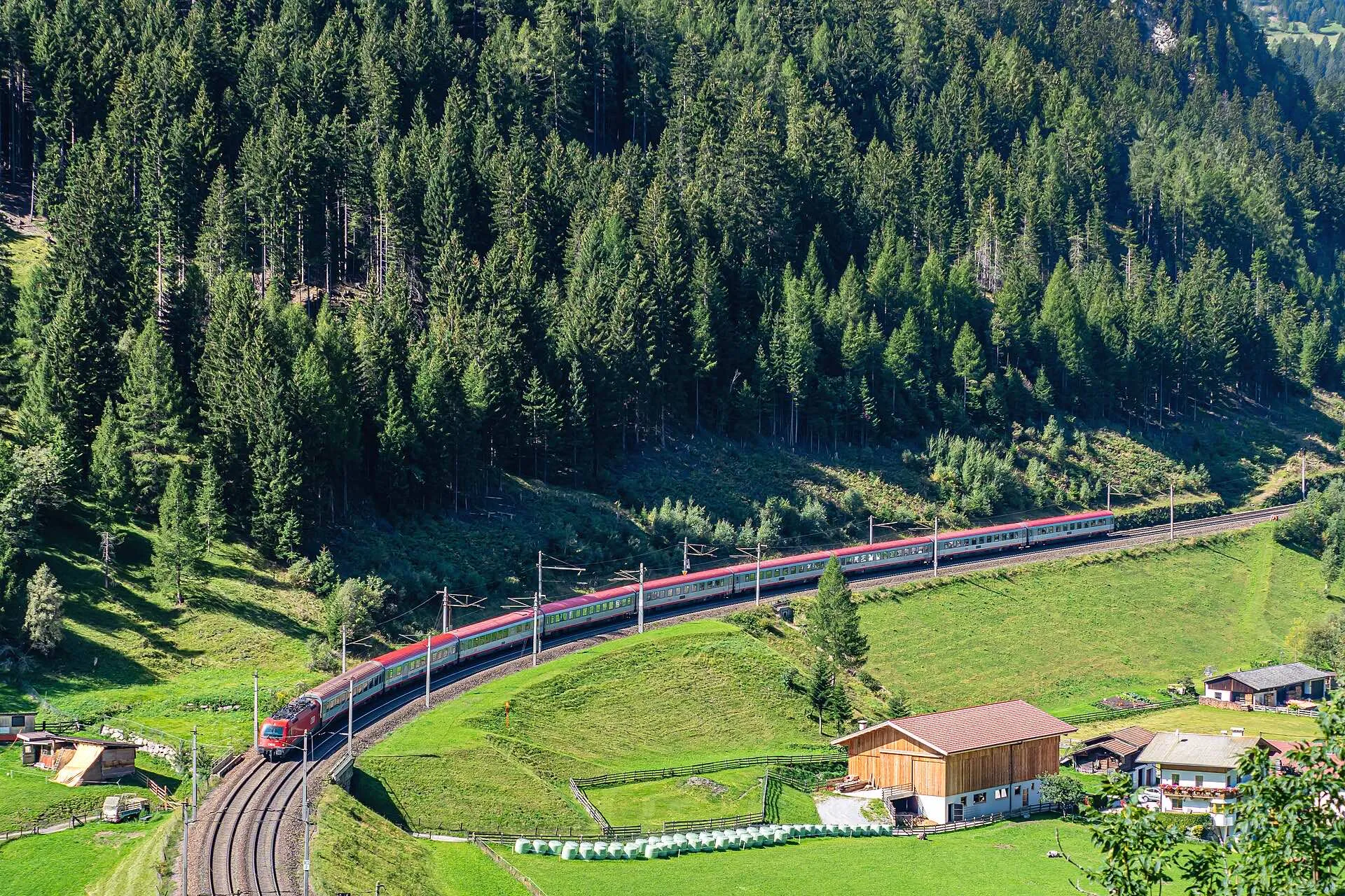 A Eurocity train on the horseshoe curve at St. Jodok with the village and mountains behind.