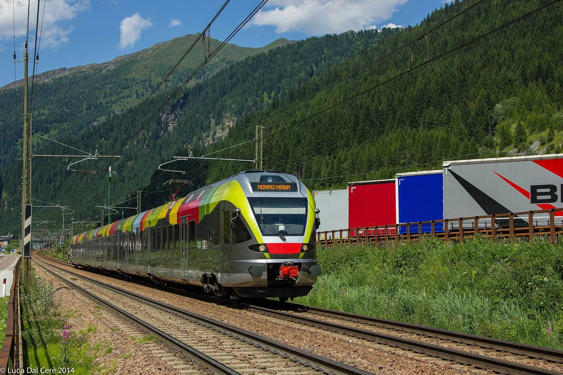 A colourful South Tyrol Flirt regional train running beside a freight train on the Brennerbahn.