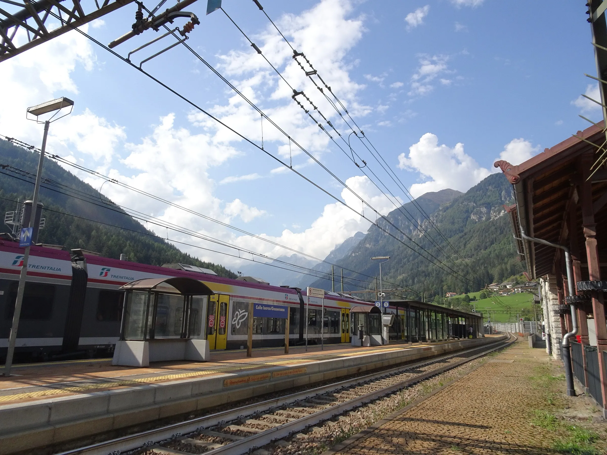 A Trenitalia regional train at the platform of Gossensass station on the Brennerbahn with mountains behind.