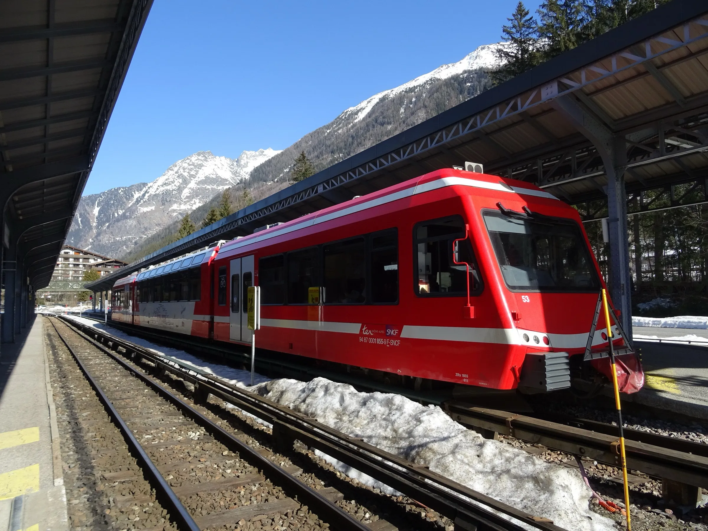 A red and white Mont-Blanc Express train at the platform of Chamonix-Mont-Blanc station with snowy peaks behind.