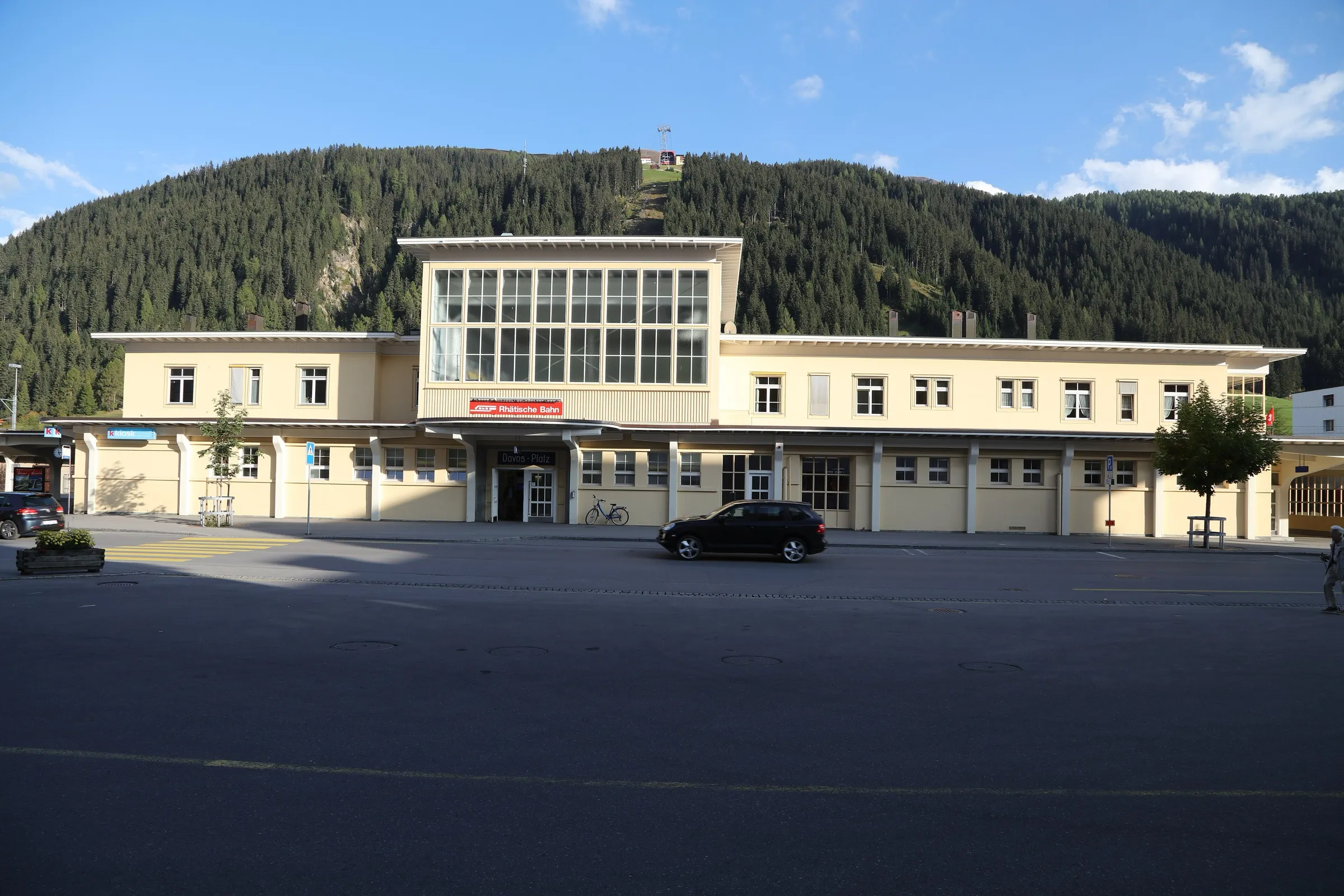 The yellow station building of Davos Platz with a forested hillside behind it.
