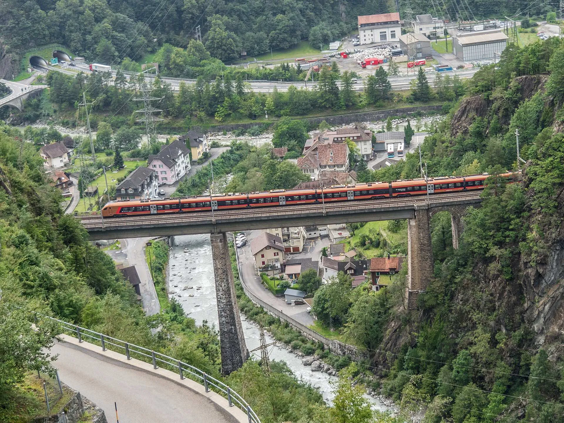 A copper coloured SOB train crossing the high Chärstelenbach bridge above Amsteg with the village below.