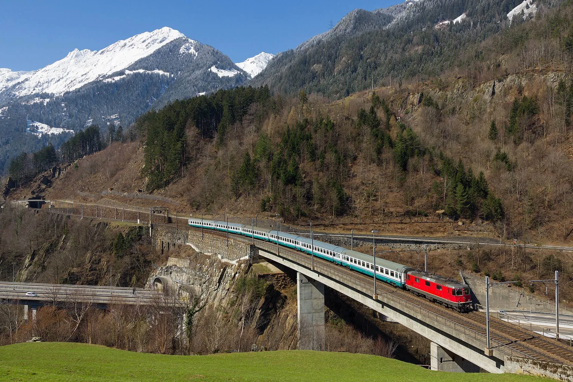 An SBB passenger train crossing the Intschireuss bridge with snowy peaks behind.