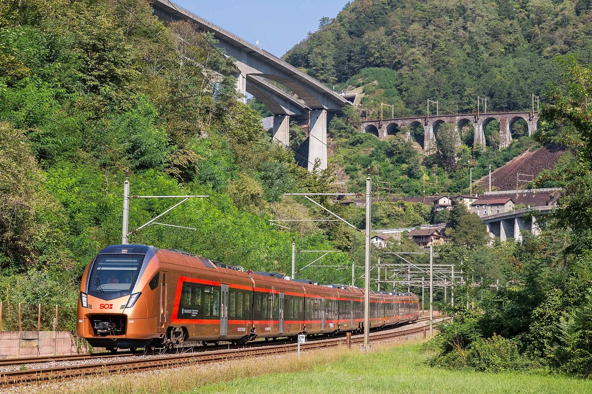 A copper coloured SOB Treno Gottardo train below the Biaschina loops near Giornico with viaducts above.