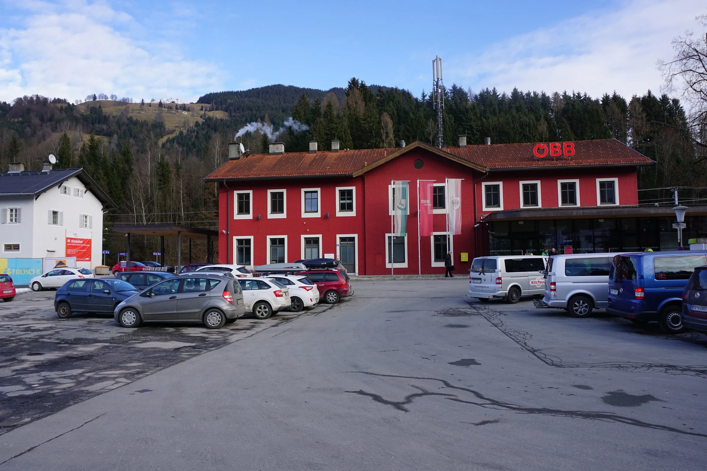 The red station building of Kitzbühel with its forecourt and wooded hills behind.