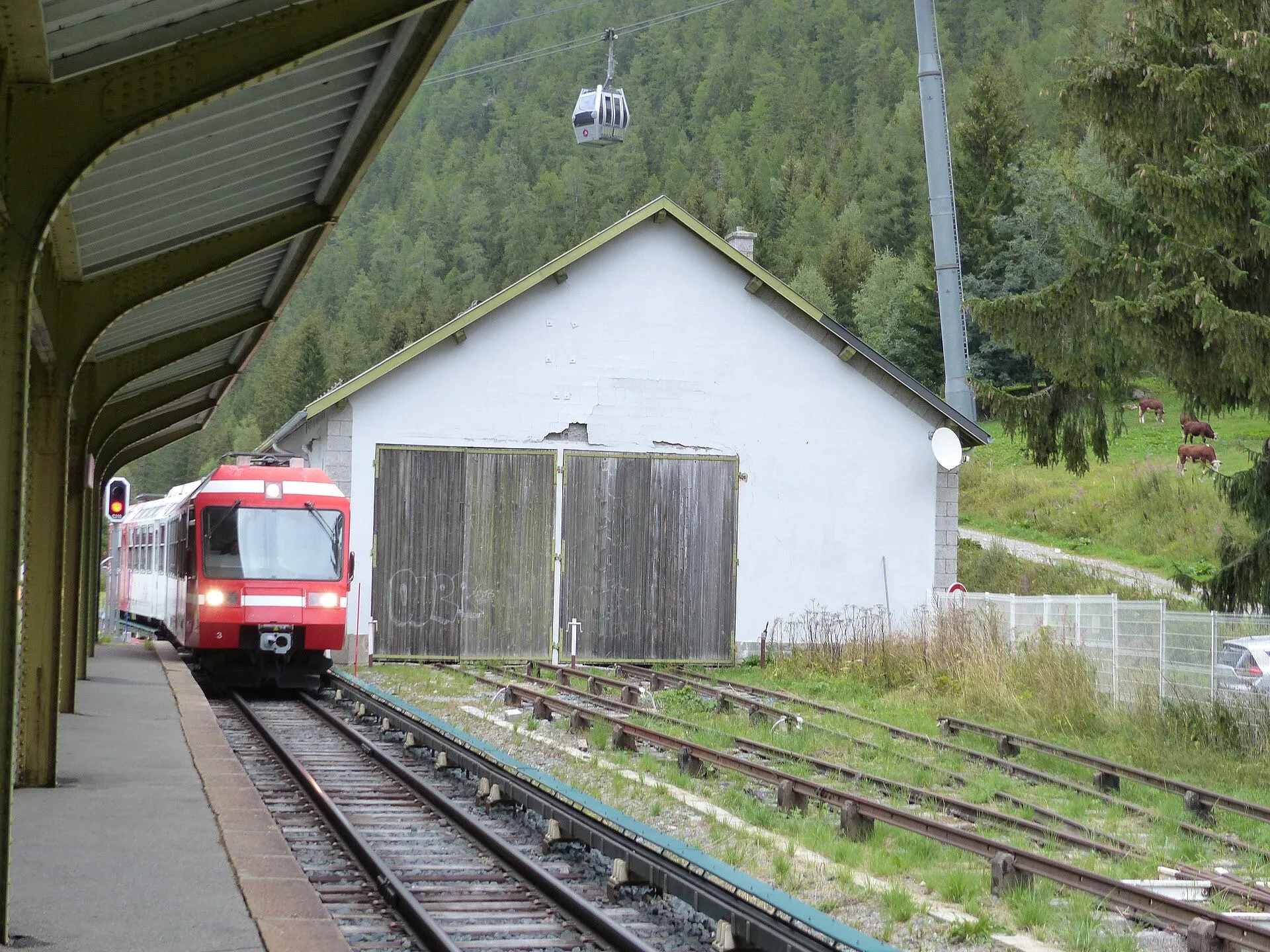 A red and white Mont Blanc Express train at the platform of Vallorcine station below forested slopes.