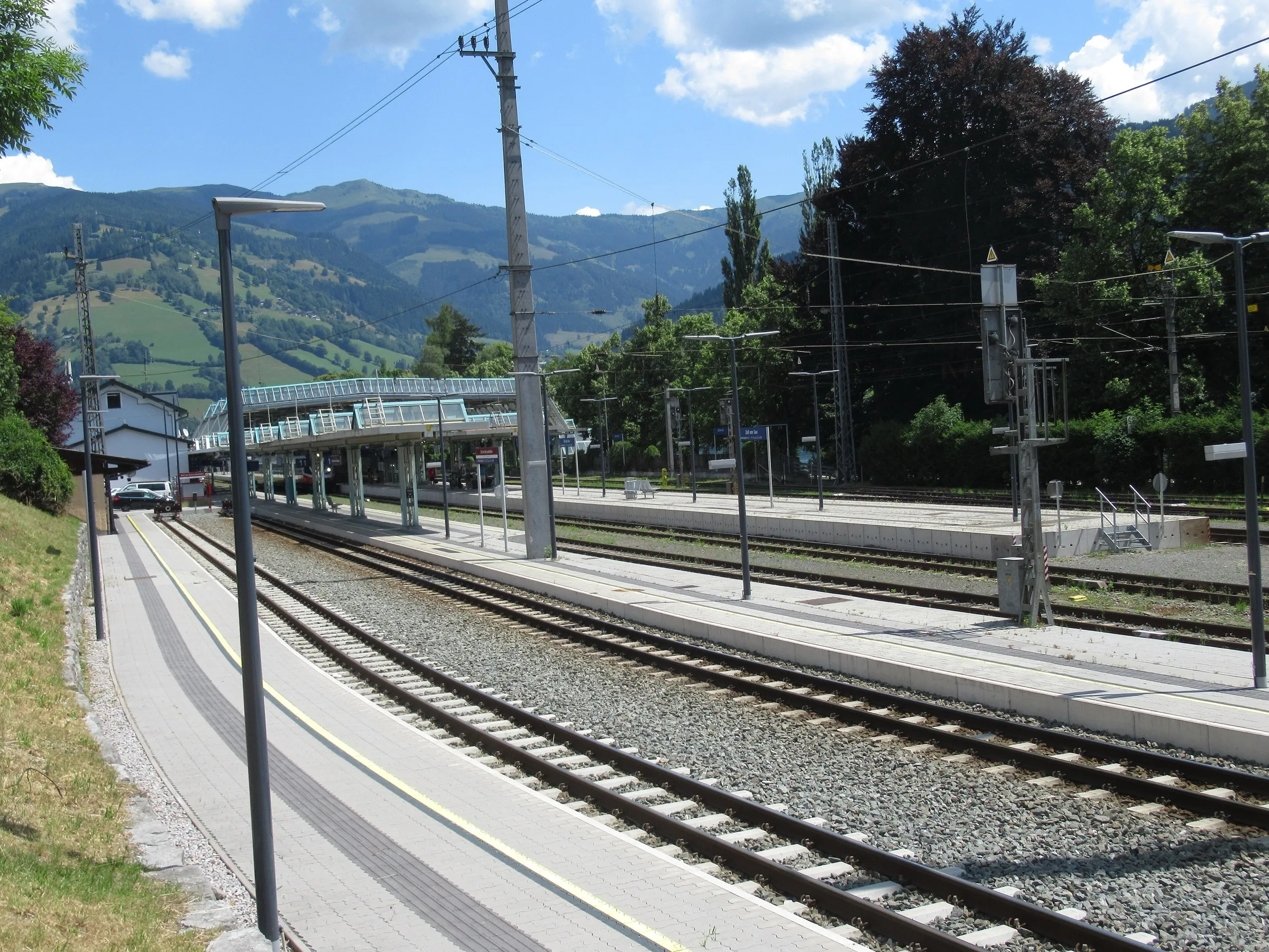 Empty platforms and tracks at Zell am See station with green hills and the footbridge beyond.